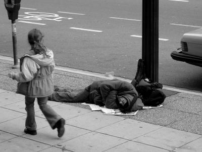 Auf diesem Bild, erkennt man einen Mann, der auf wenigen Zeitungen, am Straßenrand auf dem Boden liegt, und schläft.
